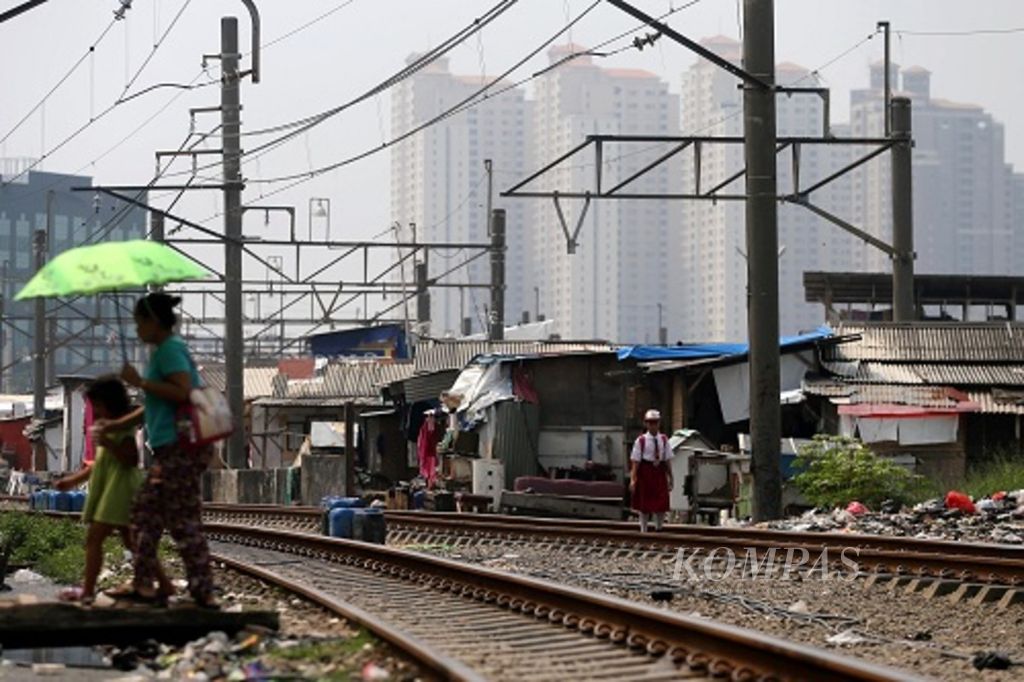 Warga melintasi bangunan semipermanen yang dibangun berjajar di sepanjang rel kereta api di kawasan Kampung Bandan, Jakarta Utara, dengan latar belakang deretan gedung hunian bertingkat, Selasa (23/5/2017). 