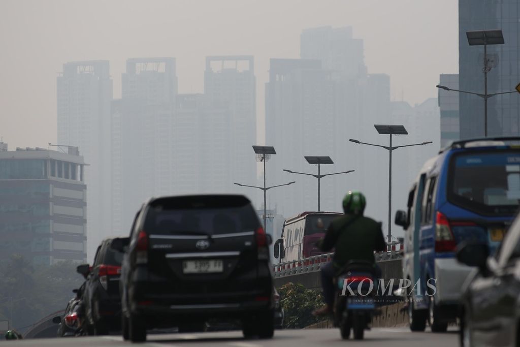 Kendaraan melalui jalan layang Slipi dengan latar belakang gedung-gedung bertingkat yang diselimuti asap polusi udara di kawasan Jakarta Barat, akhir Juli 2024.