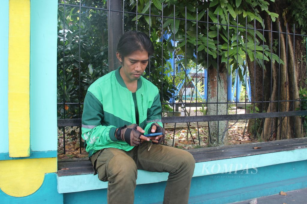 Salah satu pengendara ojek daring sedang menunggu orderan pelanggan di salah satu lokasi di Kota Pontianak, Kalimantan Barat, Selasa (19/3/2024). Pengendara ojek daring berharap ada tunjangan hari raya Lebaran tahun ini di tengah sepinya orderan dan kondisi ekonomi yang tidak mudah dihadapi.