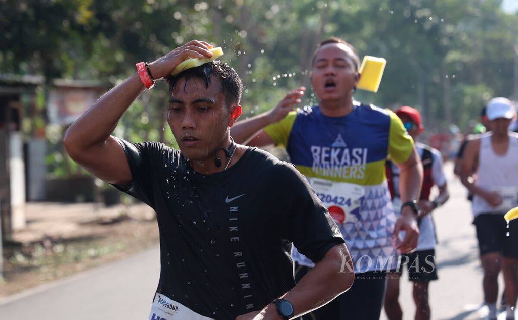 Pelari <i>half marathon</i> mendinginkan tubuhnya dengan spons pada ajang Borobudur Marathon 2023 Powered by Bank Jateng di kawasan Candi Borobudur, Kabupaten Magelang, Jawa Tengah, Minggu (19/11/2023).