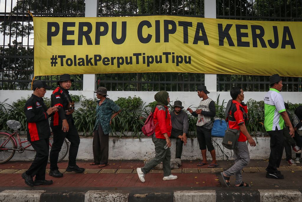 Peserta aksi melintasi spanduk penolakan Perppu Cipta Kerja di depan Gedung Parlemen, Jakarta, Selasa (28/2/2023). Ribuan massa yang terdiri dari buruh, mahasiswa, dan sejumlah elemen masyarakat menggelar aksi penolakan terhadap Peraturan Pemerintah Pengganti Undang-Undang (Perppu) Nomor 2 Tahun 2022 tentang Cipta Kerja. Mereka menilai Perppu Cipta Kerja sebagai bentuk kesewenang-wenangan pemerintahan Presiden Joko Widodo dalam memfasilitasi investor atau pemodal. ADRYAN YOGA PARAMADWYA (Z20) 28-02-2023