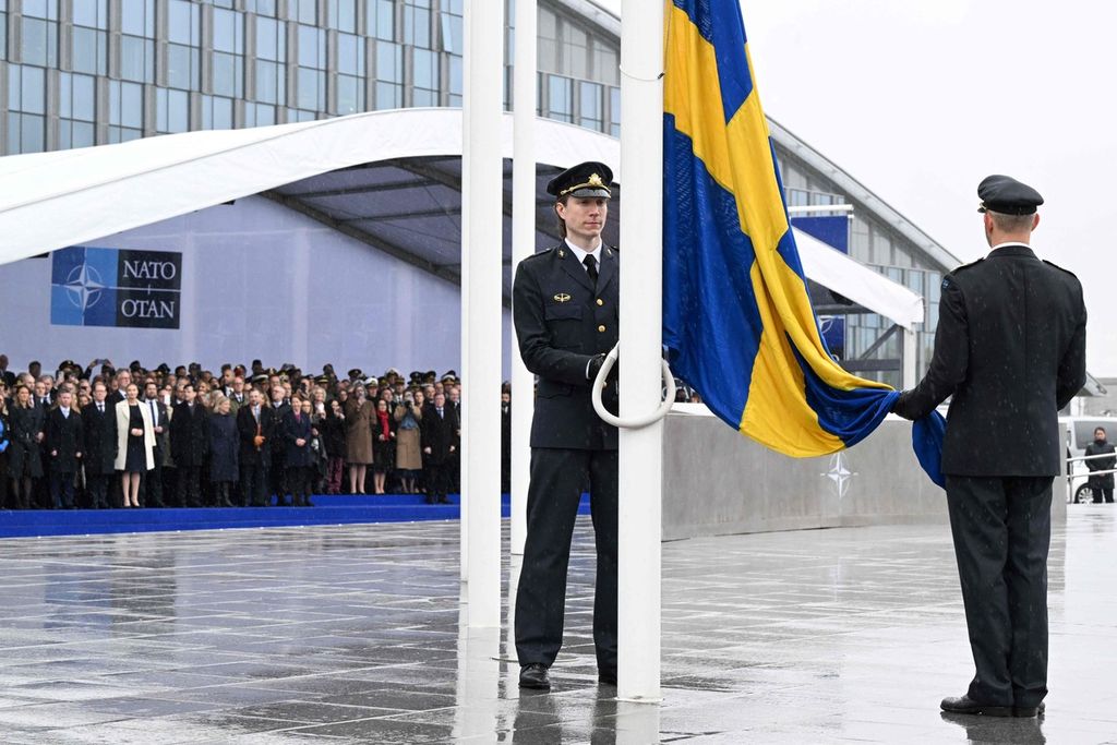 Dua personel militer bersiap mengibarkan bendera Swedia di markas NATO di Brussels, Belgia, Senin (11/3/2024). Bendera Swedia telah dikibarkan di markas NATO menandai secara resmi negara ini bergabung sebagai anggota ke-32.  