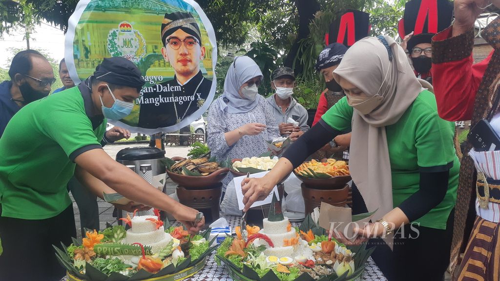 Sejumlah warga makan bersama nasi tumpeng di luar gerbang Pura Mangkunegaran, Kota Surakarta, Jawa Tengah, Sabtu (12/3/2022). Pesta rakyat itu digelar secara swadaya untuk menyambut penobatan Gusti Pangeran Haryo Bhre Cakrahutomo Wira Sudjiwo sebagai Kanjeng Gusti Pangeran Adipati Arya Mangkunegara X.