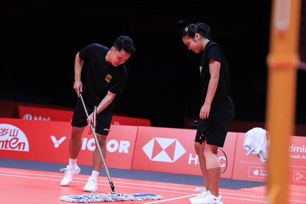 Gregoria Mariska Tunjung (kanan) mengamati Anthony Sinisuka Ginting mengeringkan lapangan saat berlatih di Hangzhou Olympics Sports Center, China, pada Senin (11/12/2023). 