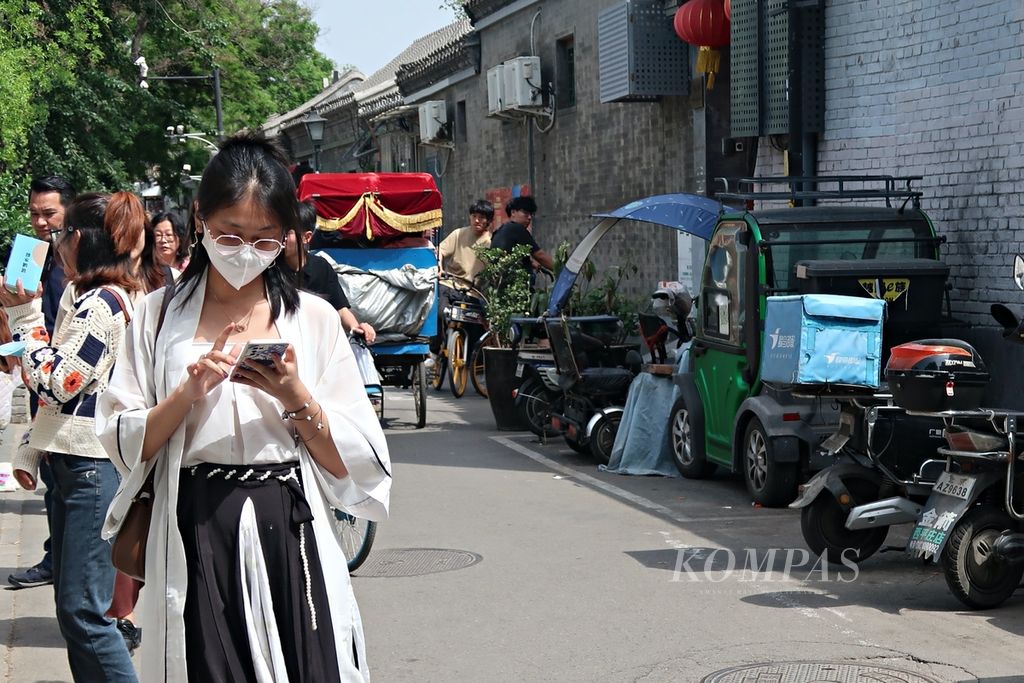Seorang warga China terlihat berjalan di pusat kota Beijing sembari memegang ponsel pintar saat berkunjung ke Nanluoguxiang atau South Luogu Lane di Distrik Dongcheng di Beijing, China, Selasa (2/5/2023).