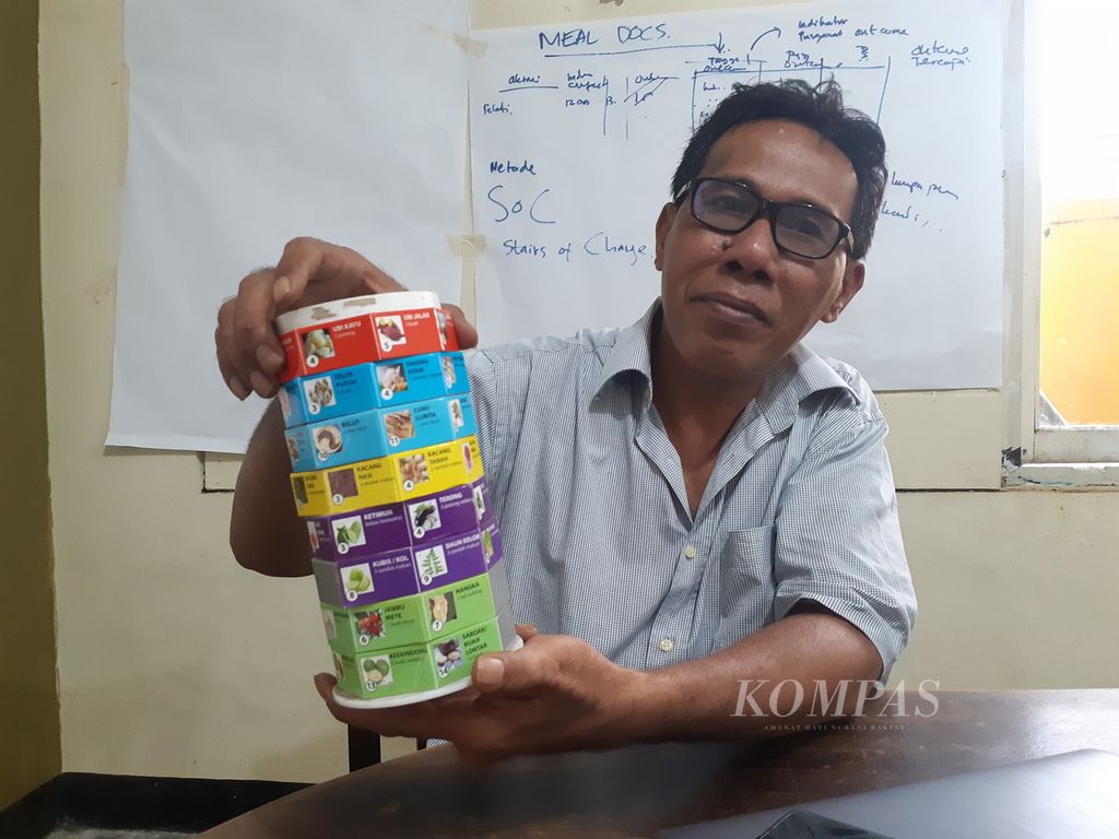 Zadrak Mengge dari Yayasan Penguatan Lingkar Belajar Komunitas Lokal (Pikul) menunjukkan alat peraga bernama Pelangi Meja, Selasa (21/3/2023). Pada alat peraga itu tertulis jenis makanan beserta kandungan nutrisinya. Jenis makanan dimaksud ditemukan di sejumlah perkampungan di Nusa Tenggara Timur.
