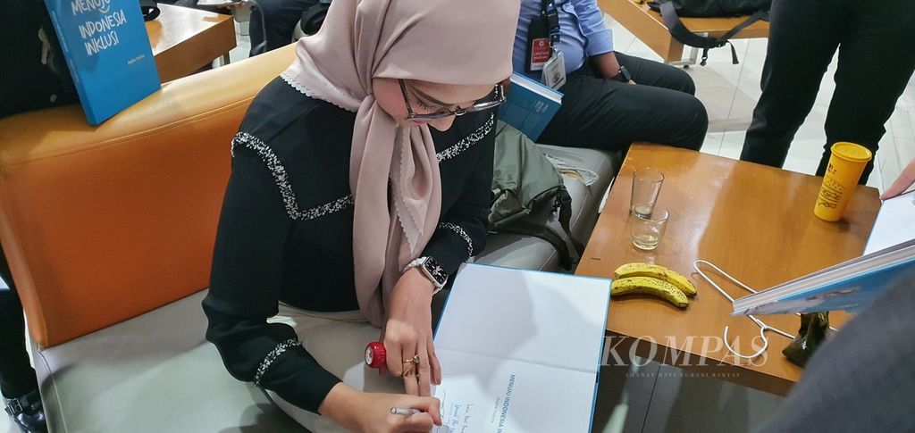 Angkie Yudistia membubuhkan tanda tangan pada bukunya yang diberikan kepada para wartawan peliput di Istana Kepresidenan, Jakarta, Rabu (26/7/2023).