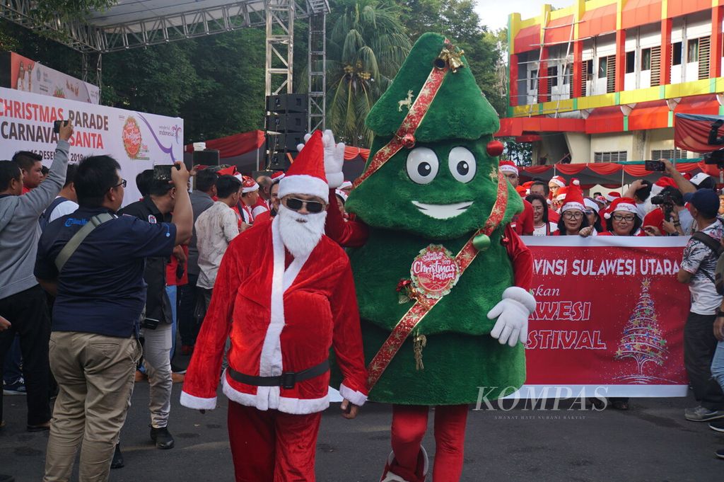 Stenly Walangitan, aparatur sipil negara (ASN) dari Inspektorat Sulawesi Utara yang berdandan menjadi sinterklas, berjalan bersama maskot Festival Natal Sulawesi Utara dalam pawai sinterklas di Manado, Sulut, Senin (16/12/2019).