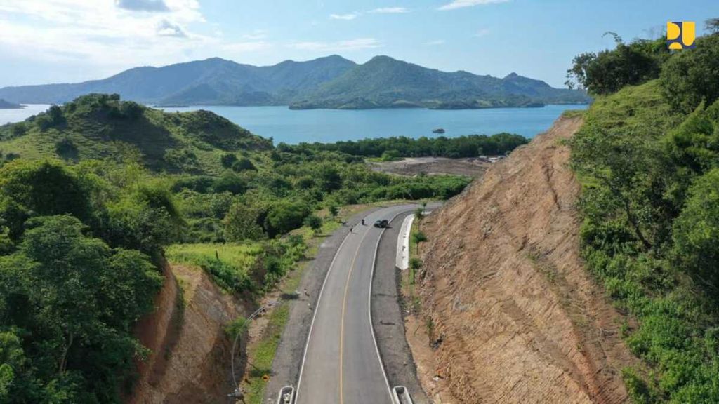 Jalur Jalan Akses Labuan Bajo-Golo Mori melintasi tepian bukit yang hijau ditambah laut yang membiru dan pulau-pulau kecil di tengahnya. 