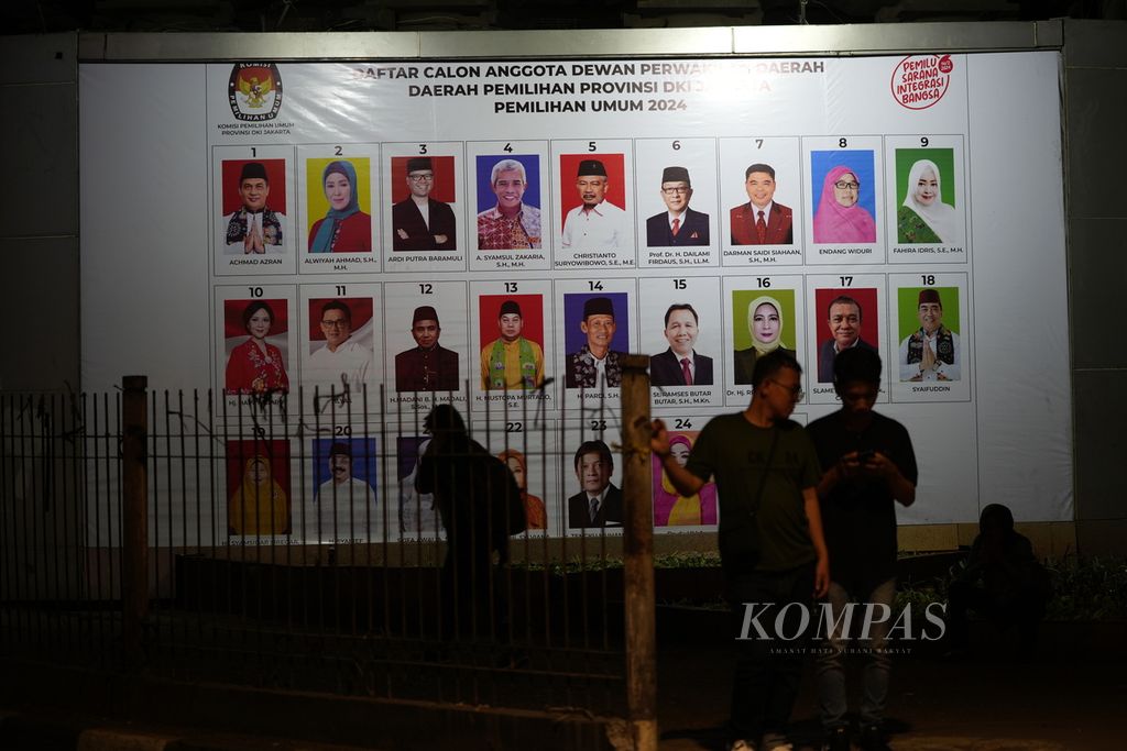 Residents cross a billboard featuring a photograph of a candidate who is running for the Regional Representative Council (DPD) member in the electoral district of DKI Jakarta Province under an overhead toll road in Slipi, Central Jakarta (9/1/2024).