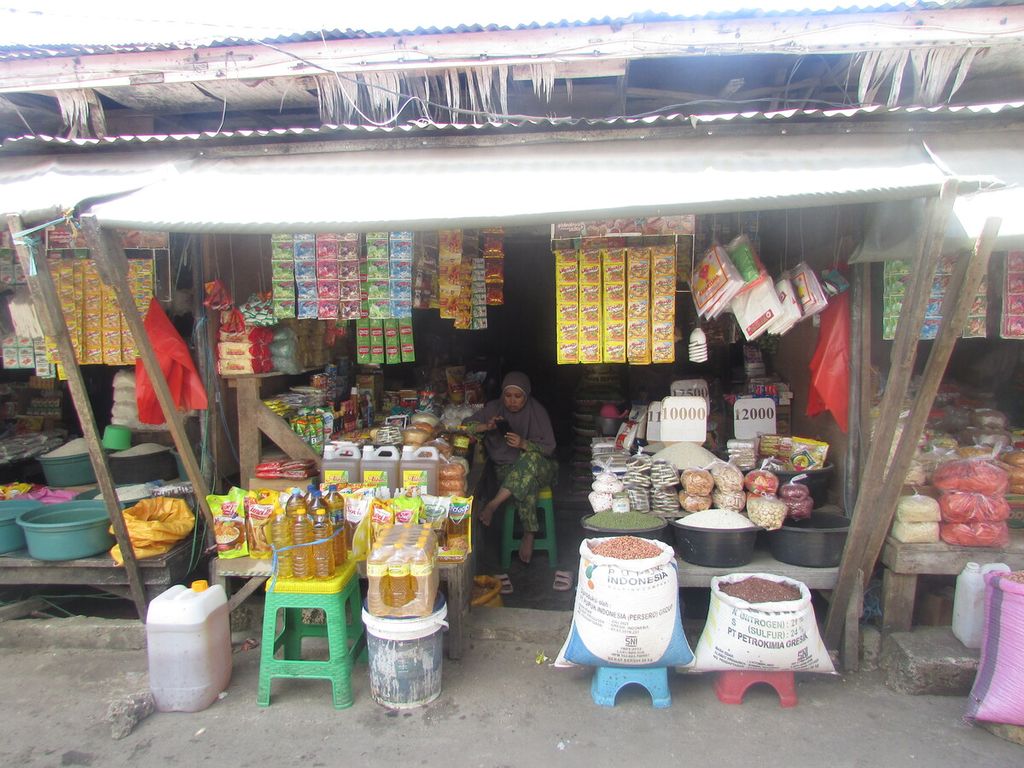 Ny Halimah duduk dalam kios miliknya di Pasar Naikoten Kupang, Senin (5/9/2022). Ia tengah serius mencari informasi di dalam ponsel pintar soal dampak kenaikan tarif BBM bersubsidi di Pulau Jawa dan Sulawesi. Barang-barang dagangan di dalam kios itu sebagian besar didatangkan dari Makassar, Sulawesi Selatan.
