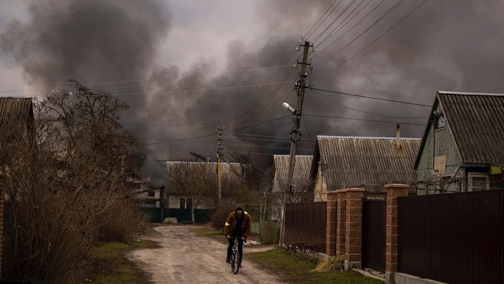 Seorang lelaki warga Ukraina mengendarai sepeda di kawasan pabrik dan toko yang terbakar akibat dibombardir militer Rusia di Irpin, tidak jauh dari ibu kota Ukraina, Kiev, Minggu (6/3/2022).