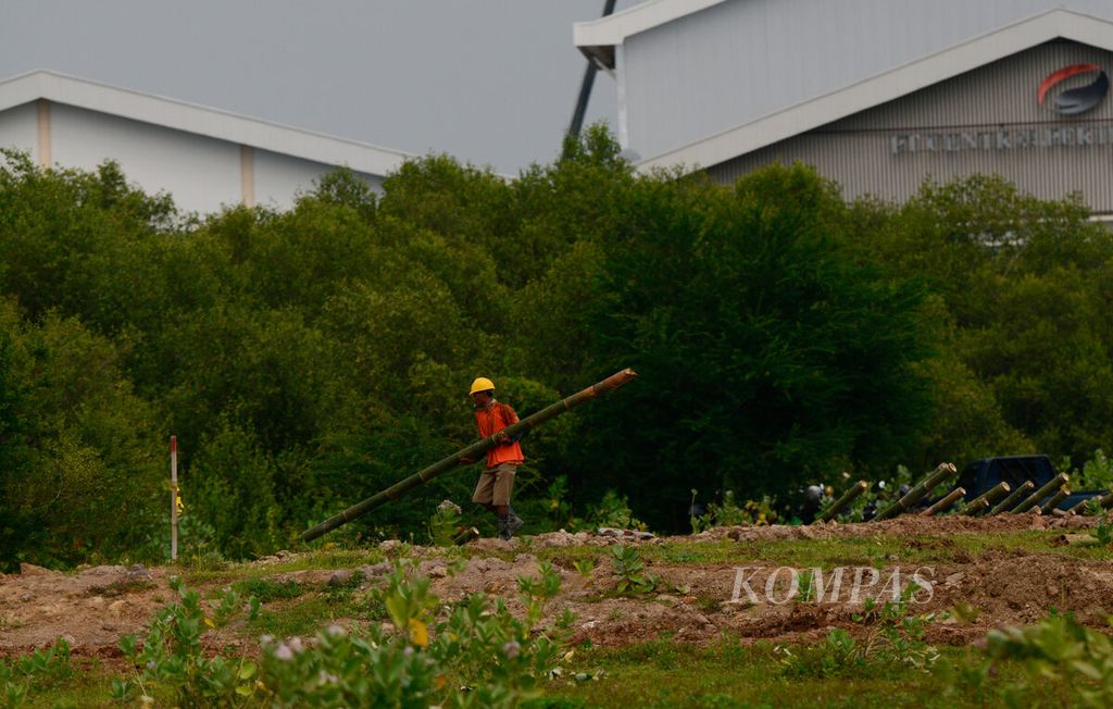 Pekerja membawa bambu untuk membuat tanggul yang membatasi lahan dengan area mangrove di Kecamatan Kaliwungu, Kabupaten Kendal, Jawa Tengah, Selasa (30/1/2024). Kawasan industri seluas 2.200 hektar tersebut mulai berkembang dengan pembangunan pabrik dari investor yang mengembangkan usahanya.