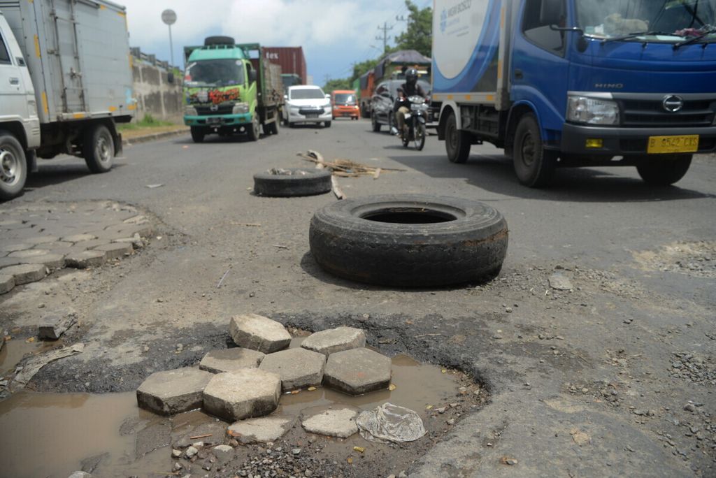 Ban bekas serta bambu yang dipasang sebagai penanda adanya kerusakan jalan di Jalan Kaligawe, Kota Semarang, Jawa Tengah, Selasa (16/2/2021). Jalan rusak dan berlubang tersebut menyebabkan arus lalu lintas tersendat.