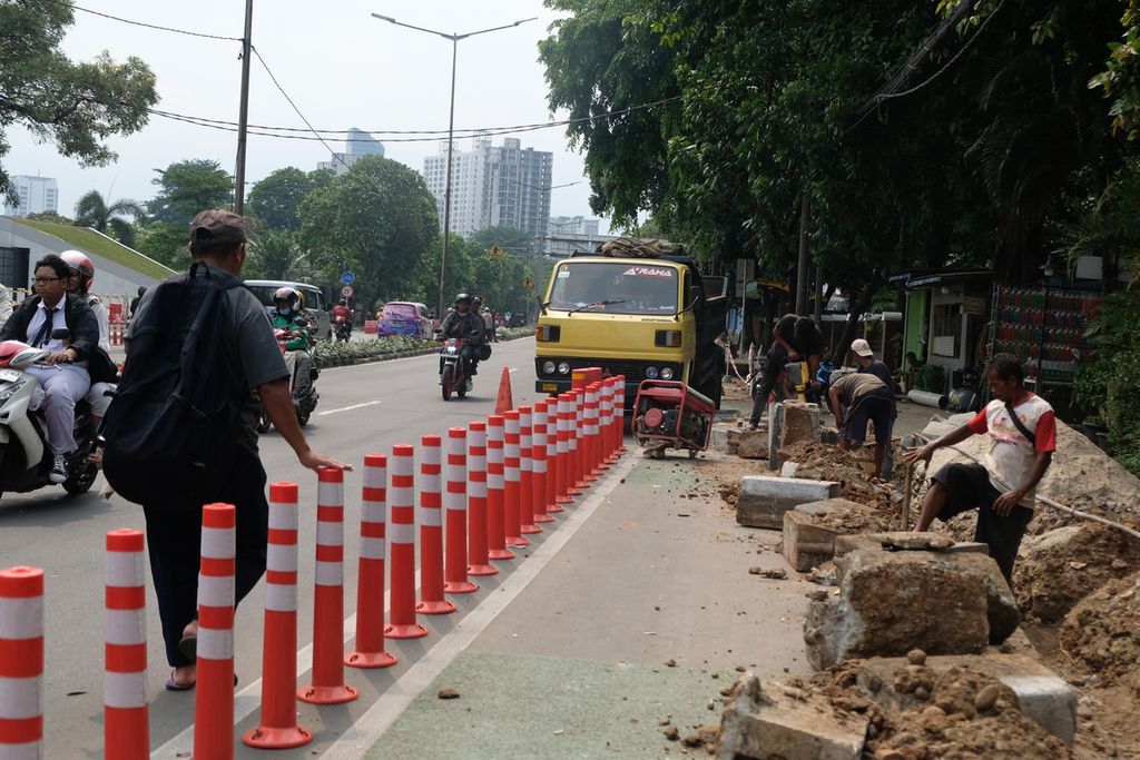 Warga berjalan di samping pengerjaan trotoar untuk pemasangan kabel listrik bawah tanah di Jalan Penjernihan 1, Jakarta Pusat, Senin (14/11/2022). Sejumlah stick cone yang terpasang sejak September lalu tersebut terlihat sudah rusak dan tidak terpasang dengan benar. 