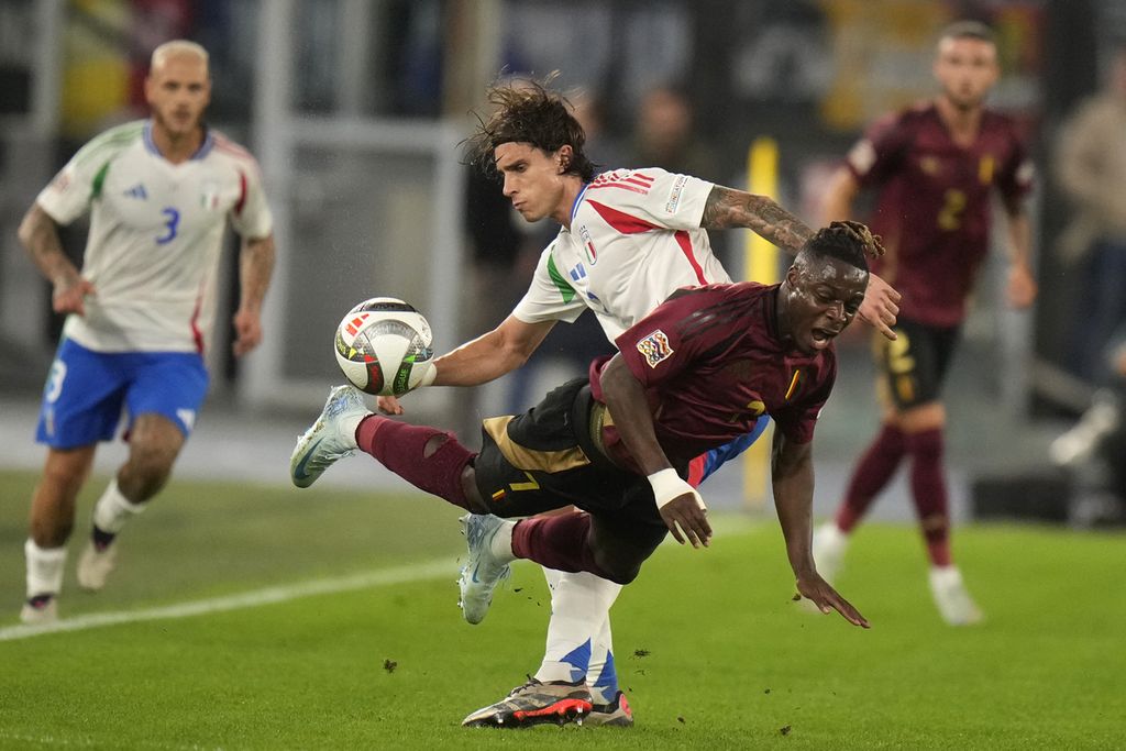 Penyerang Belgia, Jeremy Doku (tengah bawah), dijatuhkan bek Italia, Riccardo Calafiori, pada laga Liga Nasional Eropa di Stadion Olimpico, Roma, Italia, Jumat (11/10/2024) dini hari WIB. Laga itu berakhir imbang, 2-2.