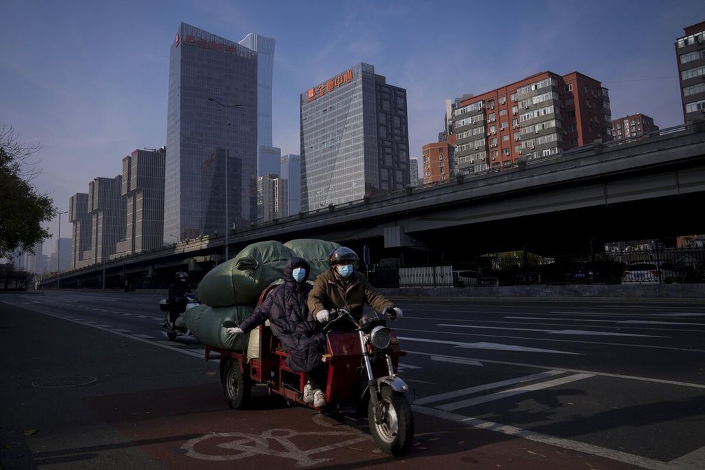 Warga mengenakan masker saat mengendarai sepeda motor yang dimuati berbagai macam barang. Mereka melintasi jalanan yang sepi di Beijing, China, 23 November 2022.