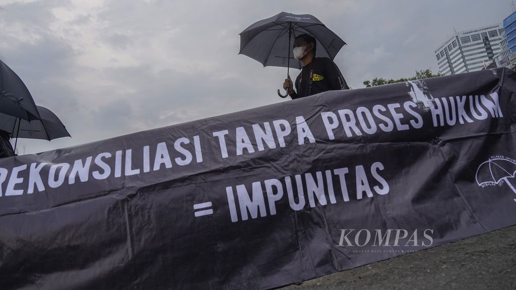 Seorang aktivis dan sebuah spanduk yang dipasang dalam Aksi Kamisan di depan Istana Merdeka, Jakarta, Kamis (1/12/2022). Aksi Kamisan rutin digelar untuk mengingatkan negara agar menyelesaikan kasus-kasus pelanggaran HAM berat masa lalu.