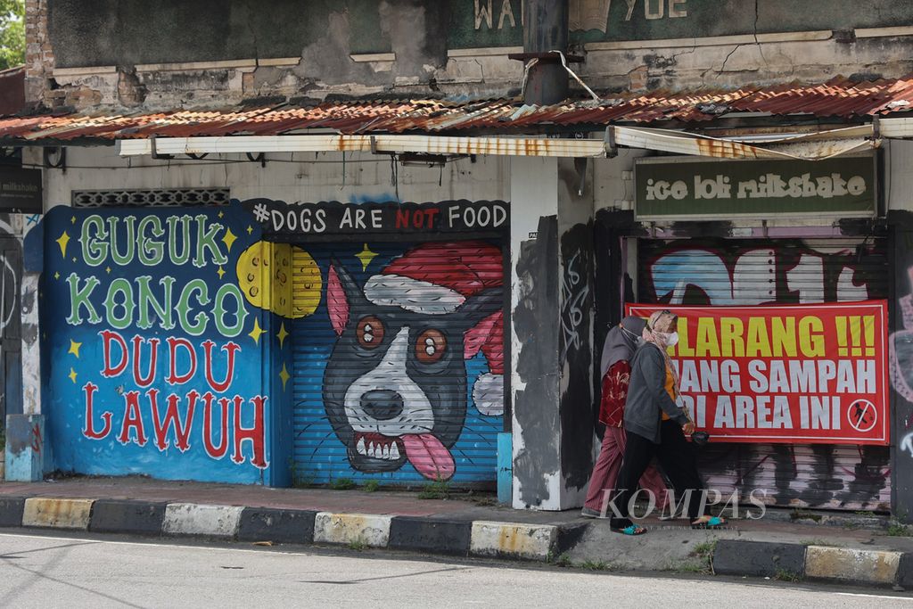 Warga melintas di depan mural tentang ajakan menghentikan praktik konsumsi daging anjing di Simpang Wirobrajan, Yogyakarta, Senin (20/2/2023). Ajakan tersebut semakin digencarkan oleh sejumlah kalangan melalui beragam media di beberapa wilayah.