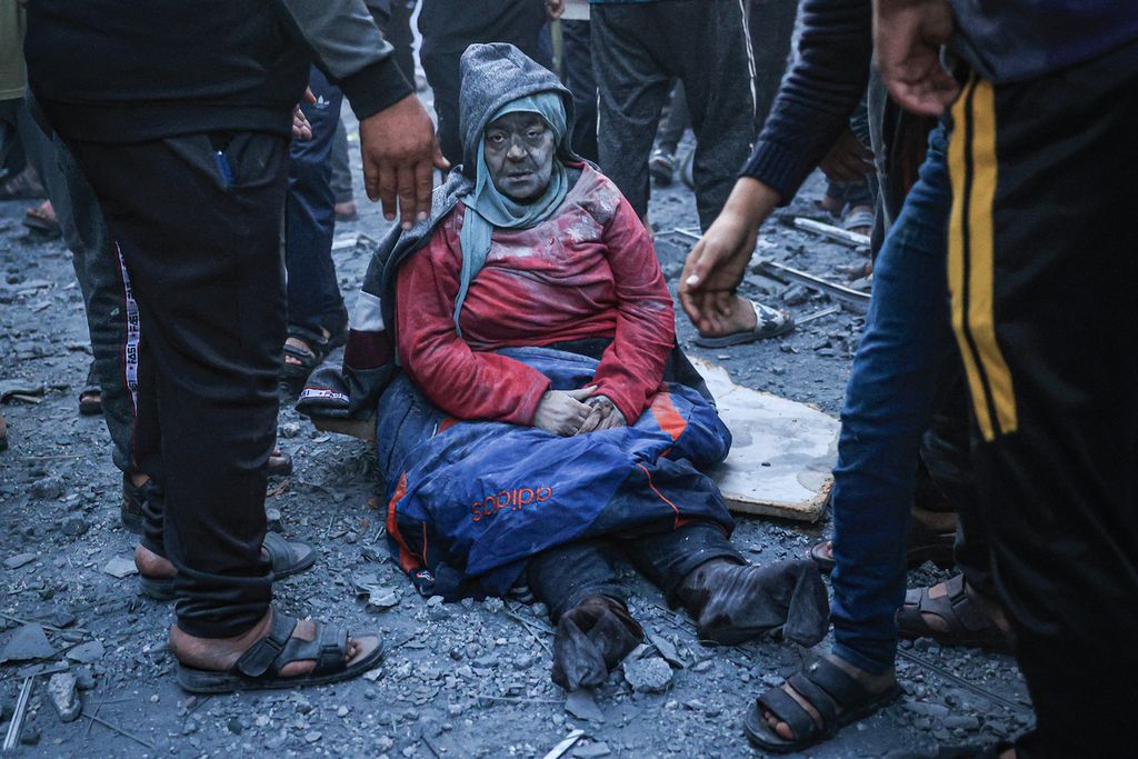 Seorang perempuan Palestina terduduk di atas tanah dengan tubuh penuh debu dan serpihan dari bangunan yang rusak ketika Israel menyerang Rafah, Gaza selatan, Minggu (3/12/2023).
