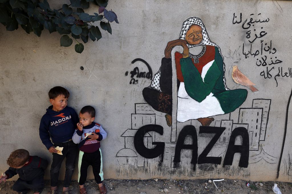 Anak-anak pengungsi Palestina berdiri di samping lukisan mural karya seniman Amal Abo di Rafah di selatan Jalur Gaza, Minggu (31/12/2023). 