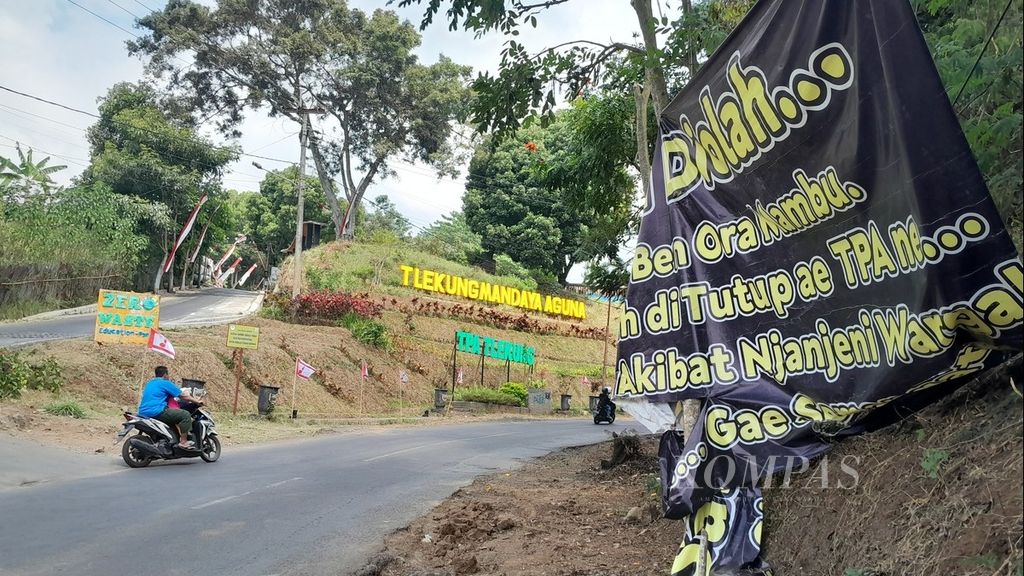 Seorang pengendara melintas di dekat spanduk yang berisi tuntutan warga terkait penanganan sampah di Tempat Pembuangan Akhir Tlekung, Desa Tlekung, Kecamatan Junrejo, Kota Batu, Jawa Timur, Minggu (6/8/2023).
