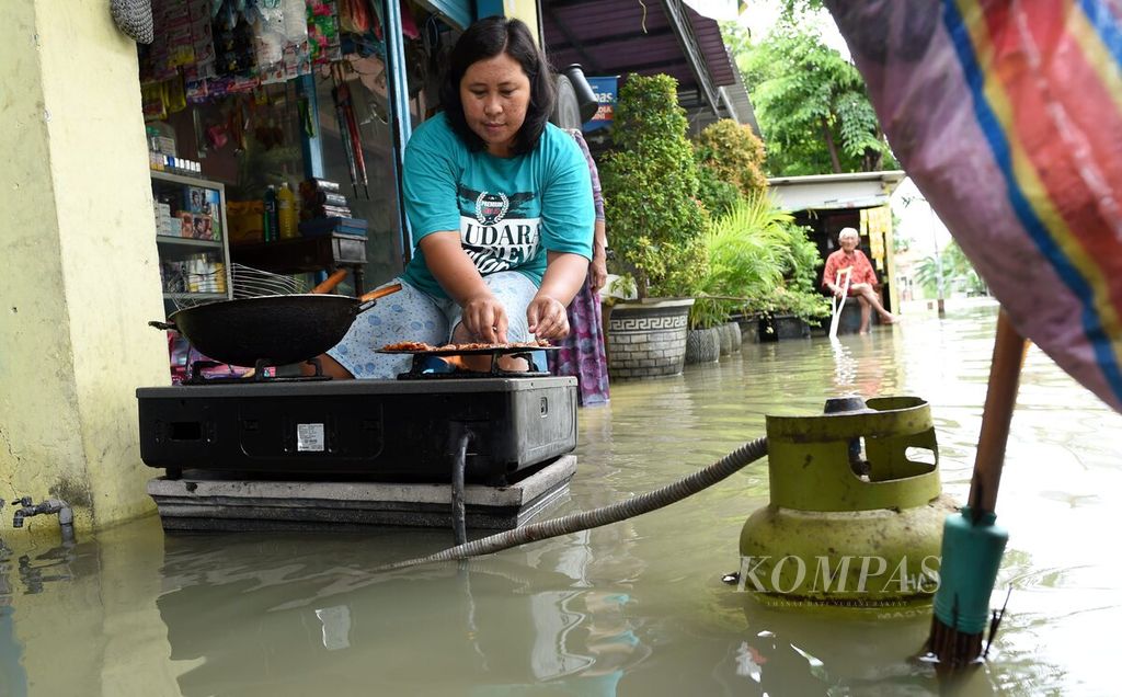 Nurlis membuat pentol bakar untuk dijual kembali di depan rumahnya saat banjir melanda Desa Morowudi, Kecamatan Cerme, Kabupaten Gresik, Jawa Timur, Selasa (15/12/2020). 