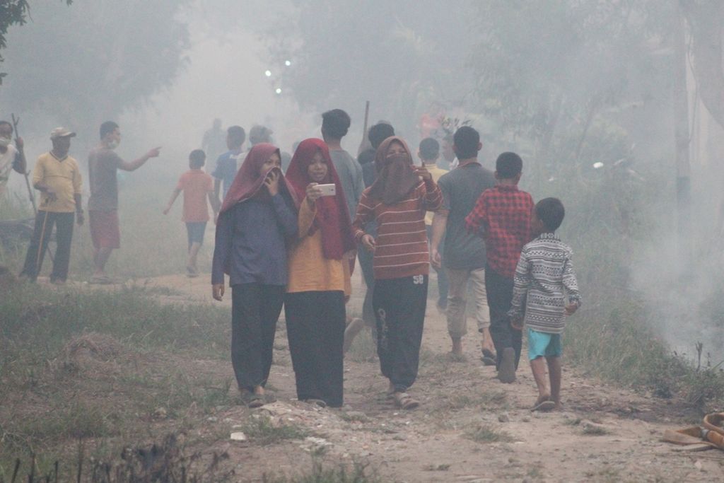 Warga melewati kepulan asap akibat kebakaran lahan di Kelurahan Sri Mulya, Kecamatan Sematang Borang, Kota Palembang, Sumatera Selatan, Selasa (15/10/2019). 