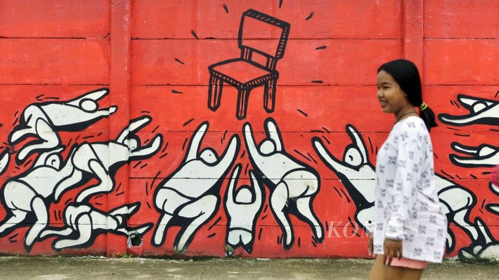Residents pass around a mural depicting people fighting for power on a wall fence in Penjaringan, Jakarta, Tuesday (21/2/2017).