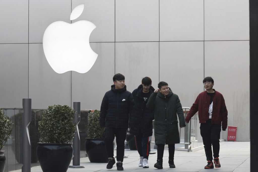 Warga melintas di belakang logo Apple di Beijing, China, Kamis (3/1/2019).