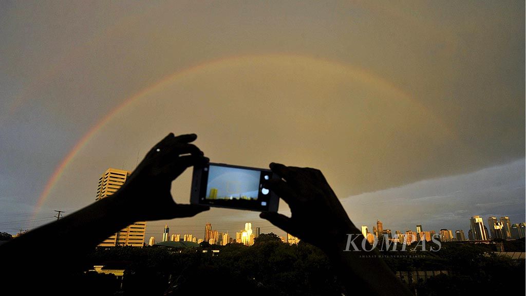 Warga mengabadikan pelangi yang muncul di atas langit Jakarta setelah hujan deras mengguyur Jakarta dan sekitarnya, Selasa (28/3) sore. Pelangi muncul karena adanya pembiasan cahaya matahari oleh butiran air hujan.