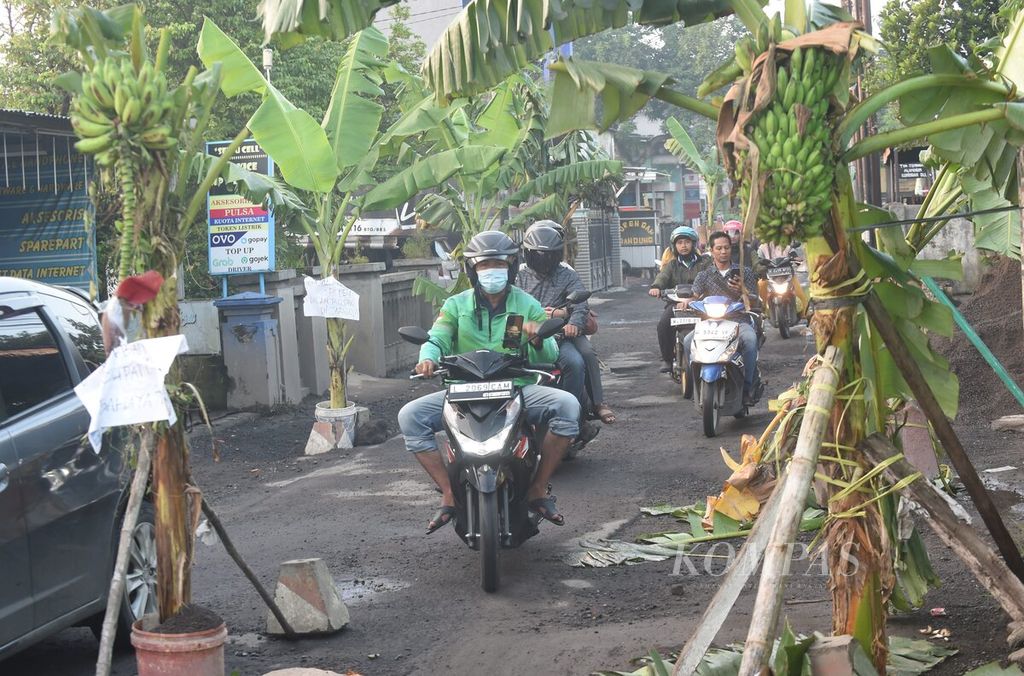 Dengan pelan-pelan pengendara sepeda motor melewati jalan rusak yang ditanami pohon pisang di Desa Jumputrejo, Kecamatan Sukodono, Sidoarjo, Jawa Timur, Rabu (20/3/3024). Karena jalan tidak juga diperbaiki, warga berinisiatif menanami jalan yang rusak dengan pohon pisang.