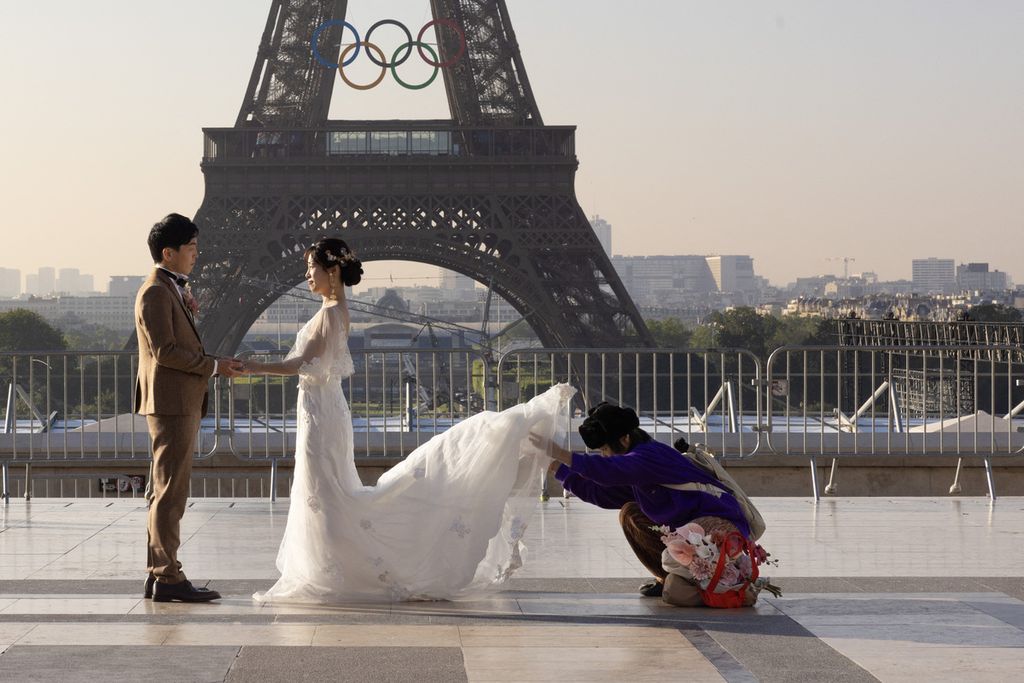 Pasangan pengantin baru bersiap berfoto dengan latar belakang Menara Eiffel di Paris, Perancis, yang telah dihiasi dengan cincin Olimpiade Paris 2024, Jumat (7/6/2024).