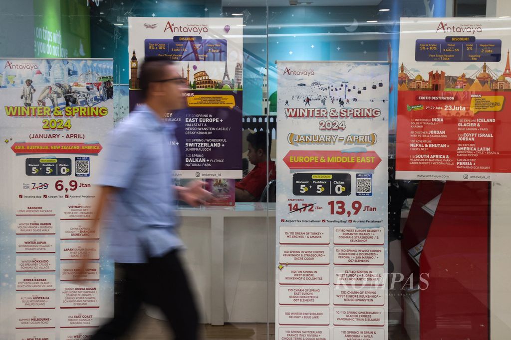 Warga melintas di depan poster promo paket wisata di salah satu biro perjalanan di Mal Kota Kasablanka, Jakarta Selatan, Selasa (19/12/2023). 