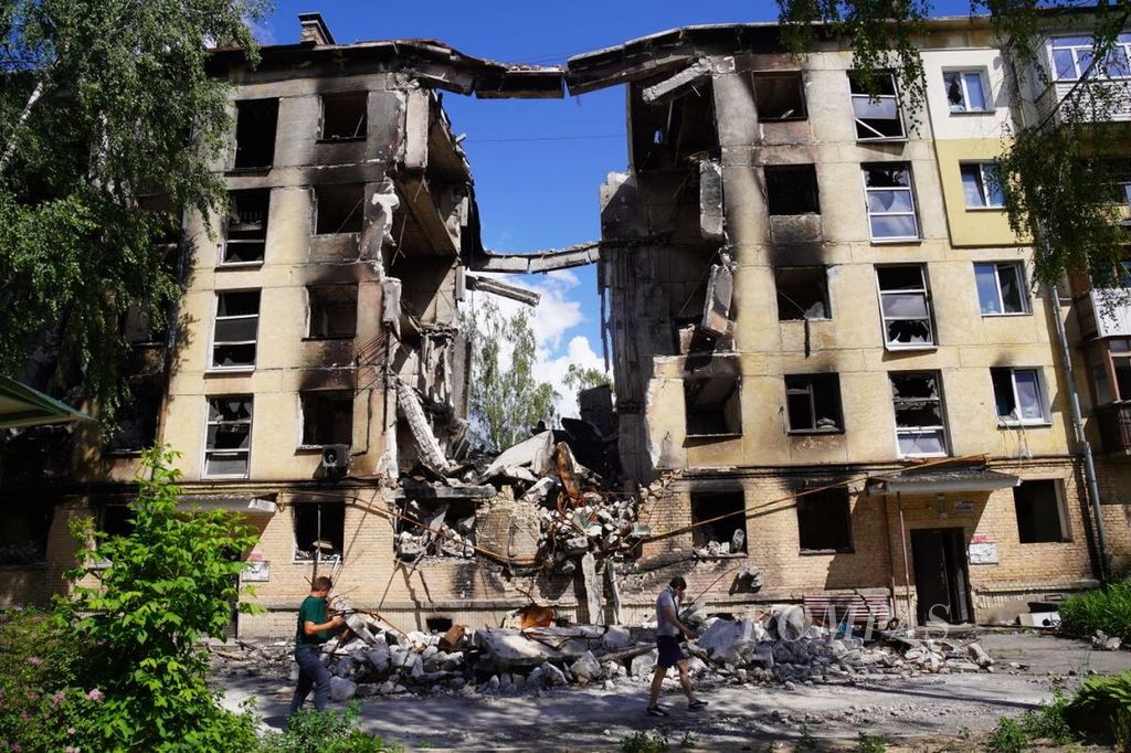 Warga melintasi gedung yang hancur dihajar rudal di wilayah Gostomel, Provinsi Kyiv, Ukraina, Sabtu (18/6/2022). Gedung ini berada di sekitar pangkalan udara Gostomel yang merupakan salah satu lokasi yang pertama kali diserang Rusia.