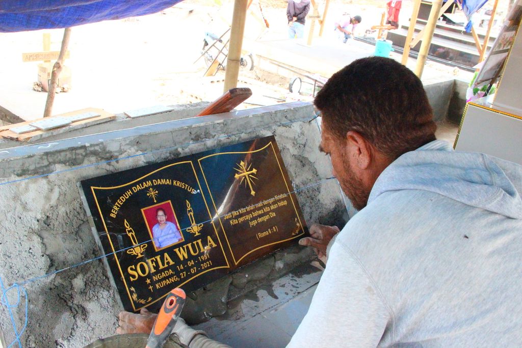 Manuak Blegur (46), tukang, memasang batu nisan pada makam Sofia Wula di tempat pemakaman khusus korban Covid-19, Fatukoa, Kota Kupang, Nusa Tenggara Timur, Selasa (10/8/2021). Sofia meninggal dengan status suspek Covid-19.