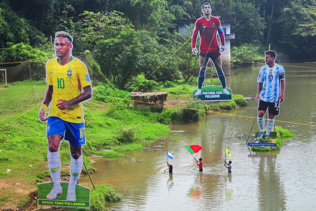 Penggemar sepak bola membawa bendera di samping poster raksasa bergambar pemain Brasil Neymar (kiri), pemain Portugal Cristiano Ronaldo (tengah), dan pemain Argentina Lionel Messi. Poster itu didirikan di tengah aliran sungai Cherupuzha di Kozhikode, Kerala, India, Senin (7/11/2022).