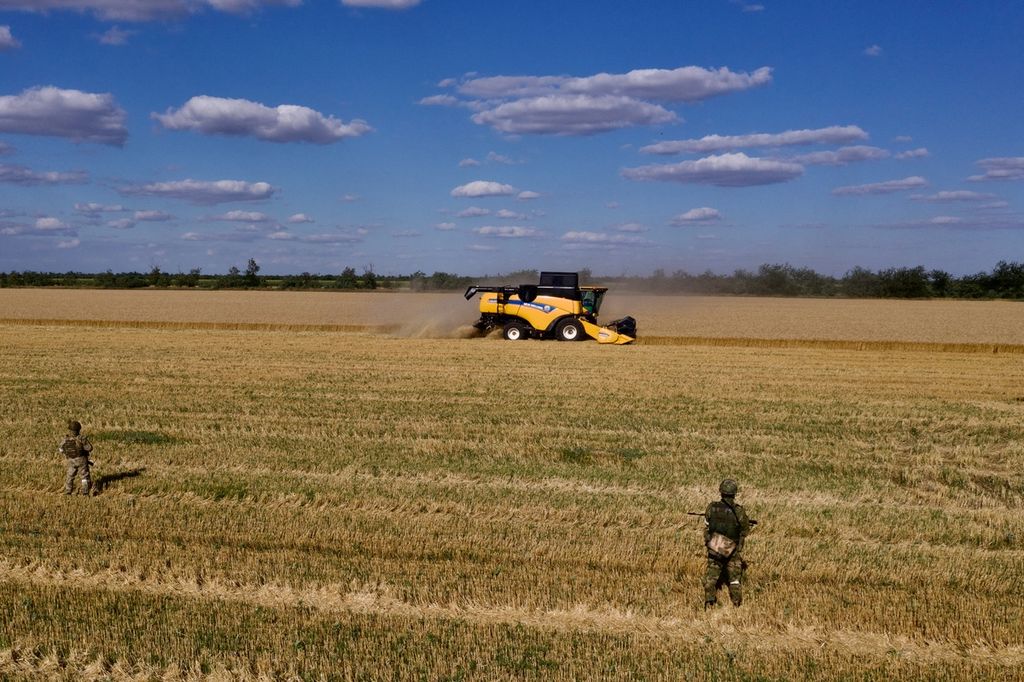 Dalam foto udara 14 Juli 2022 ini, tentara Rusia berjaga di ladang saat petani memanen gandum\ di dekat Melitopol, wilayah Zaporizhzhia, di tengah operasi militer Rusia di Ukraina. Harga pangan meningkat akibat perang Ukraina-Rusia.