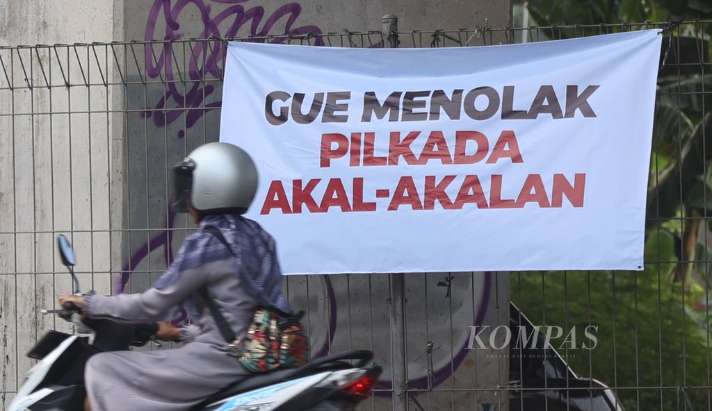 Warga melintas di dekat tulisan terkait Pilkada Jakarta di kawasan Pondok Kelapa, Jakarta, Selasa (20/8/2024).  