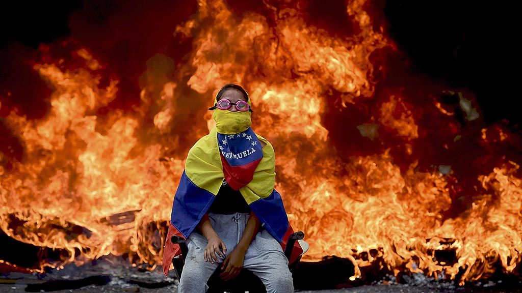 Seorang demonstran oposisi  Venezuela berpose dengan latar belakang kobaran api barikade dalam aksi menentang Presiden   Nicolas Maduro, di Caracas, Venezuela, Senin (24/4). Dalam aksi massa yang sudah  berlangsung selama tiga pekan, sebanyak 24 orang tewas.  