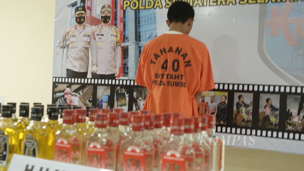 Tersangka pembuat minuman keras oplosan AM ditahan bersama minuman buatannya di Markas Polda Sumsel, Kamis (27/5/2022), di Palembang. Atas perbuatannya, AM terancam 5 tahun penjara dan denda Rp 2 miliar.