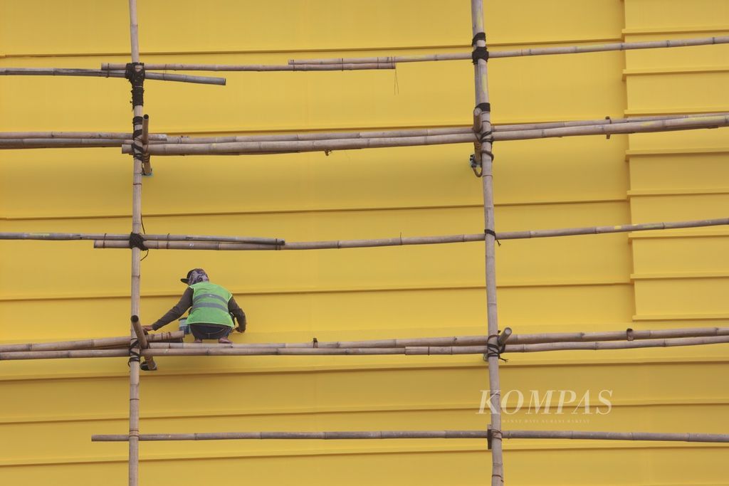 Dengan kondisi alat keselamatan kerja yang minim, para buruh bangunan bergelantungan pada tiang penyangga (steger) dari bambu untuk pengecatan dinding sebuah pusat perbelanjaan baru di kawasan Pamulang, Tangerang Selatan, Banten, Jumat (17/3/2023).  