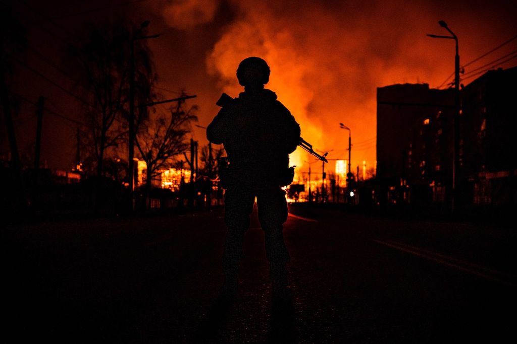 Seorang anggota pasukan khusus Ukraina tampak dalam siluet dengan latar belakang kilang gas di Kharkiv yang terbakar hebat setelah dibom Rusia, pada Rabu (30/3/2022).