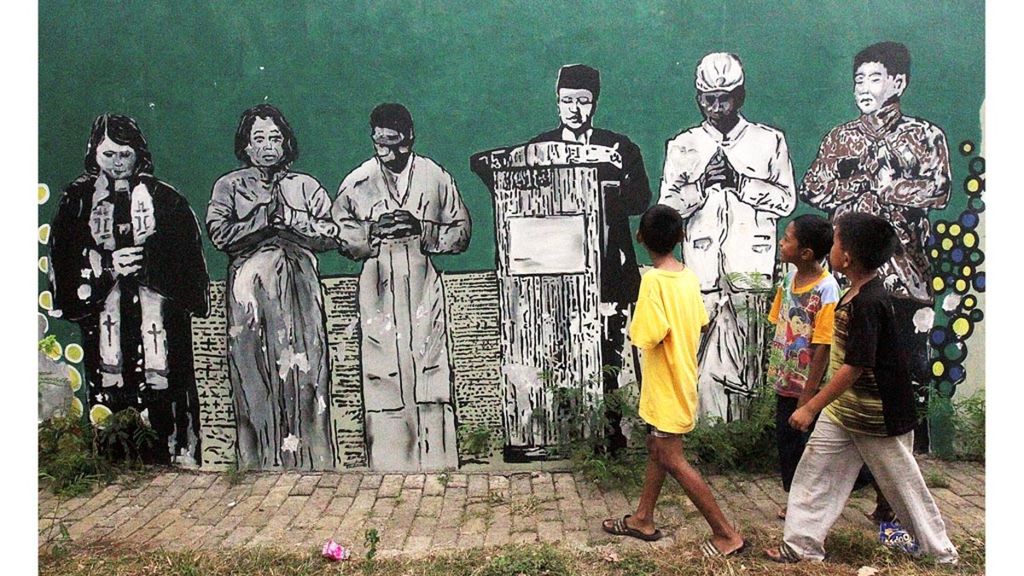 Sejumlah anak melintasi mural atau lukisan dinding yang menggambarkan kerukunan umat beragama di sepanjang tembok di wilayah Pasar Minggu, Jakarta Selatan, Minggu (2/9/2018). Kerukunan umat beragama harus terus dijaga karena menjadi modal utama pembangunan bangsa dan negara yang diproklamasikan pada 17 Agustus 1945 ini.