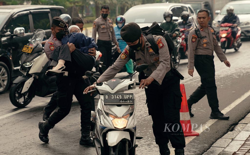 Polisi menolong pengendara sepeda motor yang tergelincir saat gerimis di Jalan Medan Merdeka Barat, Jakarta Pusat, Kamis (21/10/2021). 