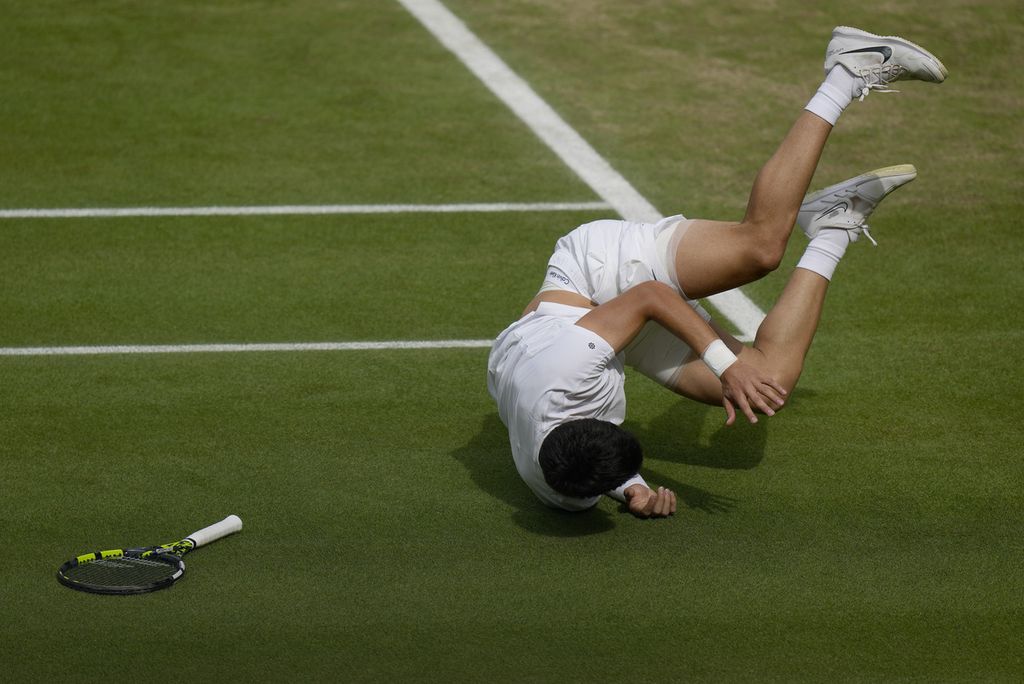 Petenis Spanyol, Carlos Alcaraz, terjatuh di lapangan saat laga final tunggal putra Grand Slam Wimbledon 2023 melawan petenis Serbia Novak Djokovic di The All England Tennis Club, Wimbledon, Inggris, Minggu (16/7/2023) malam. 
