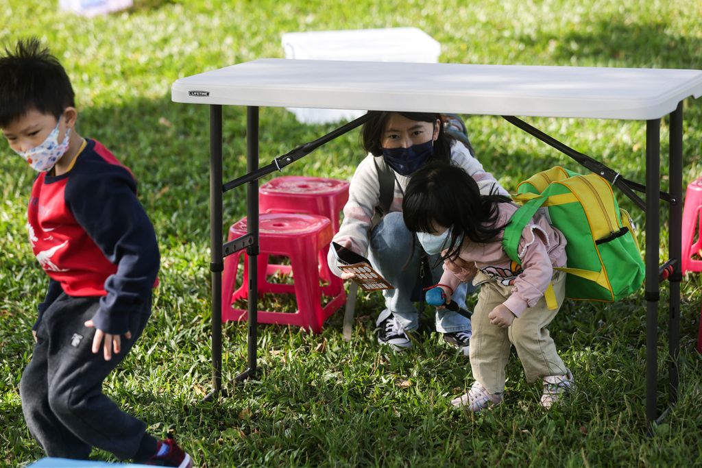 Anak-anak berlatih membawa tas berisi kotak P3K dan berjalan melewati rintangan di jalan raya dalam acara skenario latihan simulasi yang diadakan oleh organisasi pertahanan sipil Taiwan, Akademi Kuma di Kota New Taipei, Taiwan, untuk meningkatkan kesadaran akan bencana alam dan kesiapan perang, akhir November 2023.