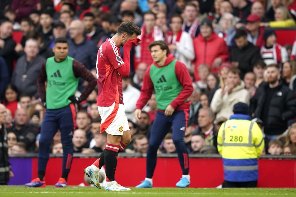 Gelandang Manchester United, Bruno Fernandes, berjalan keluar lapangan sambil menutup muka setelah mendapat kartu merah pada laga Liga Inggris melawan Tottenham Hotspur di Old Trafford, Minggu (29/9/2024). MU kalah 0-3.