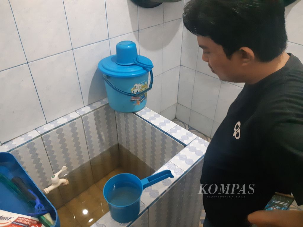 Toriq Abdullah (25) memperlihatkan air keruh yang harus ia gunakan setiap hari di Kecamatan Kalidoni, Palembang, Rabu (22/6/2022). Sudah 6 tahun air ini ia gunakan, jaringan dari PDAM Tirta Musi tak kunjung datang.