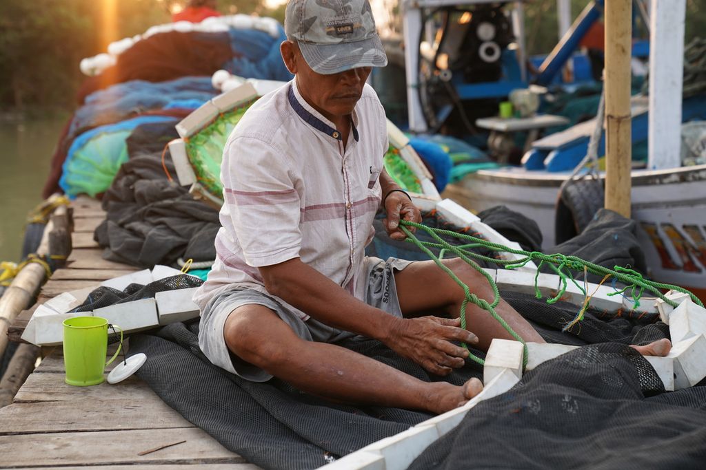 Dahuri (55) memperbaiki jaring kapal di Pelabuhan Gebang, Kabupaten Cirebon, Jawa Barat, Minggu (30/7/2023). Penghasilan Dahuri dari melaut Rp 50.000-Rp 100.000 per hari. Penghasilan rendah menjadi salah satu pemicu warga lokal untuk bekerja ke luar negeri.